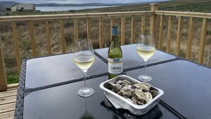 Una mesa con dos copas de vino blanco, una botella de vino y una bandeja de ostras en una terraza con vistas panorámicas.