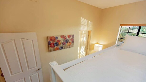 A bedroom with a bed, a door, a painting, and a window.