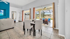 A spacious living area with a dining table, chairs, and a sofa. There are large windows offering a view of the outdoors.