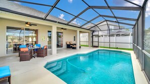A covered outdoor swimming pool with lounge chairs and a ceiling fan.