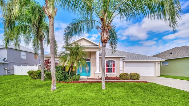 A residential house with a well-maintained lawn, palm trees, and a garage.