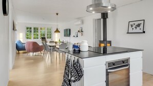 Una cocina moderna con una isla central, un comedor con sillas y vistas al exterior a través de amplios ventanales.