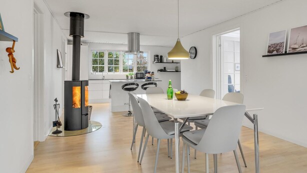 Una cocina moderna con una isla central, un comedor con mesa blanca y sillas grises, y una estufa visible con campana extractora.