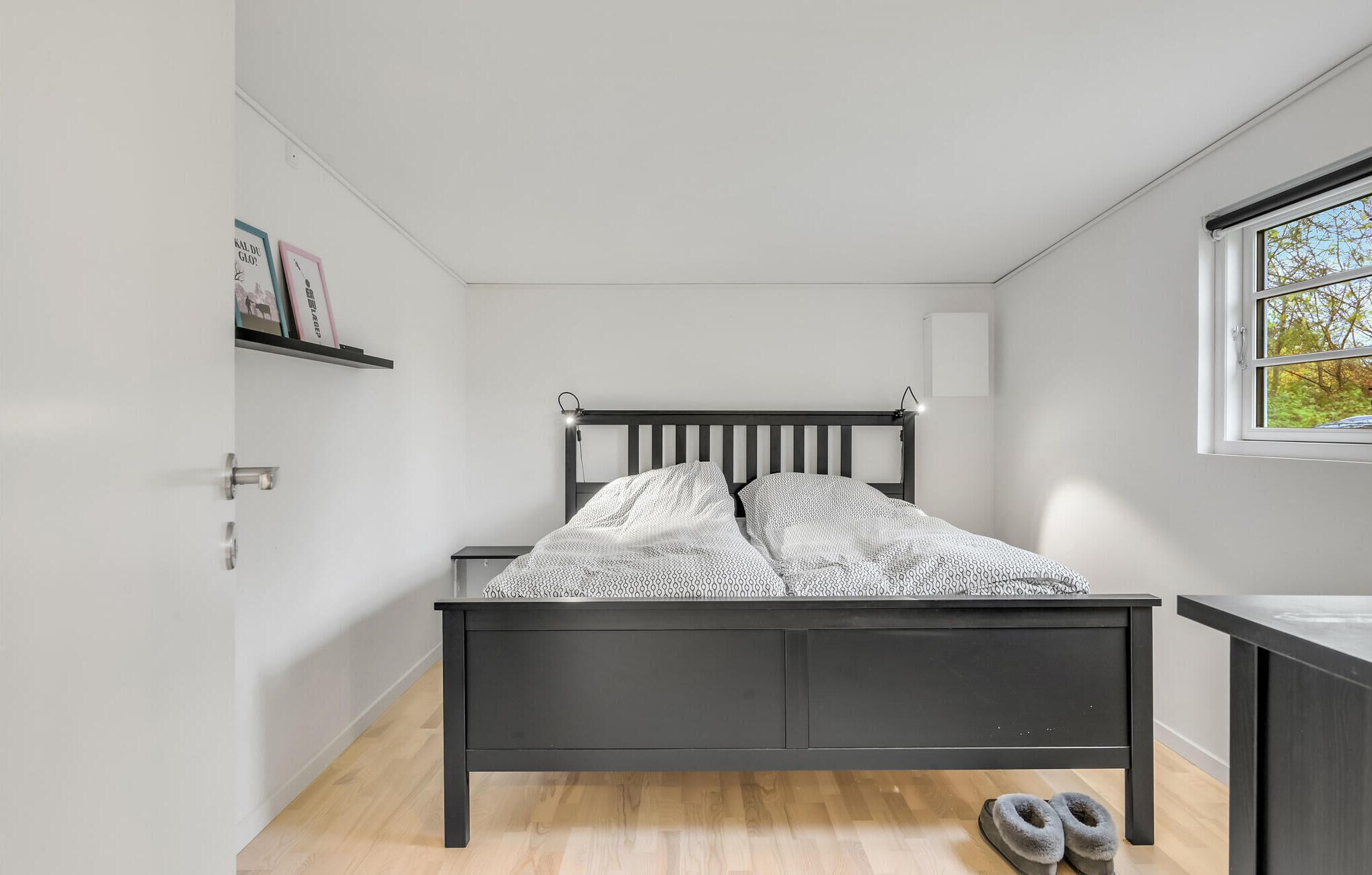 A bedroom with a bed, a nightstand, a window, and a door.