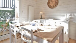 A dining area with a wooden table and chairs, a wall-mounted clock, and a window overlooking a garden. - 1 bedroom stunning apartment in Cabourg (Cabourg)