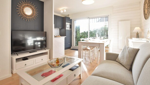 A modern living room with a flat-screen TV, a glass coffee table, and a sofa. There's a dining area with a table and chairs, and a kitchen with dark cabinets and a large window. - 1 bedroom stunning apartment in Cabourg (Cabourg)