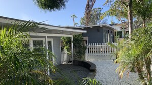 A house with a covered patio, a white picket fence, and various tropical plants. - Sweet cottage home close to beaches, airport and other attractions (San Diego)