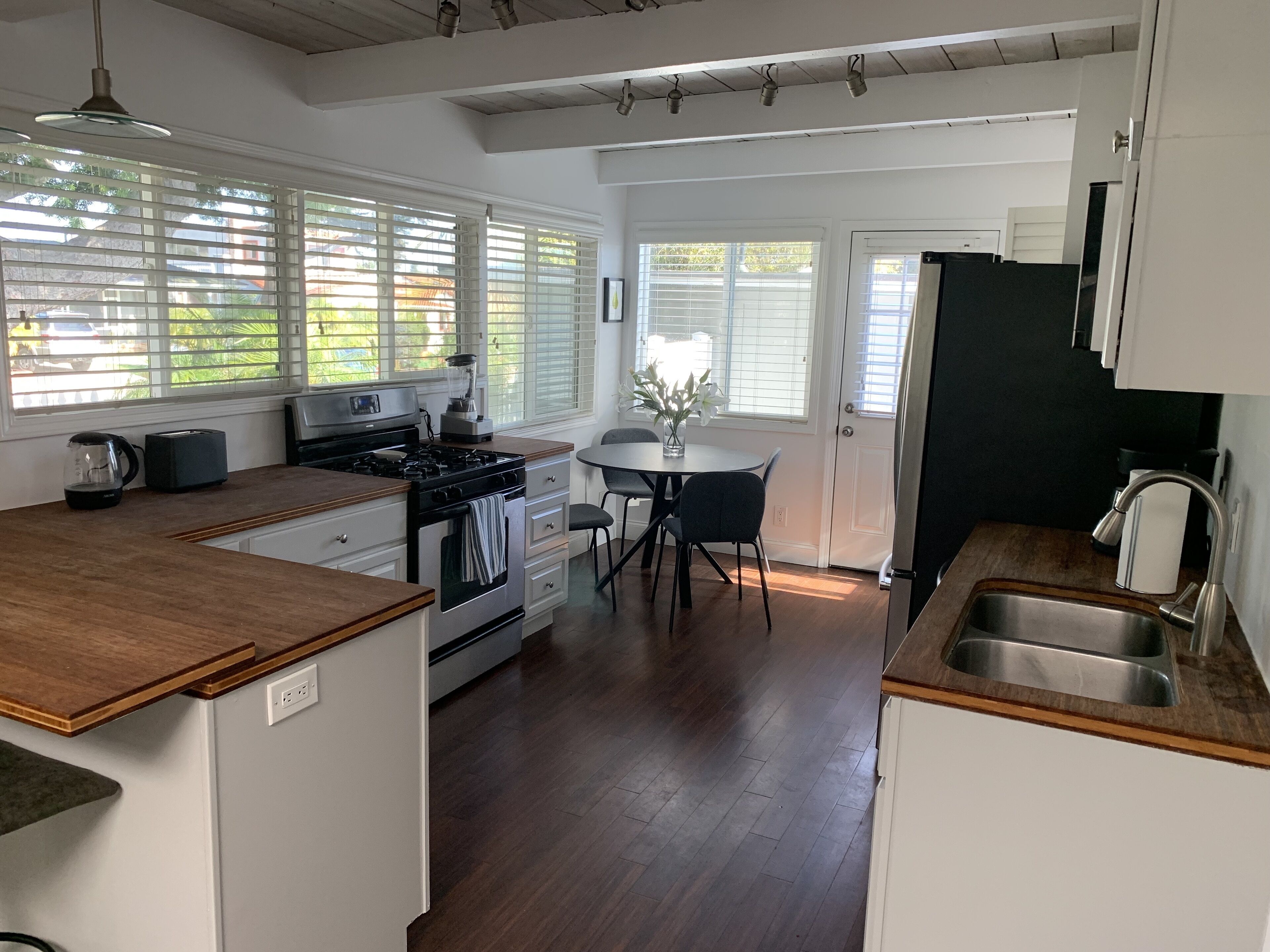 Uma cozinha moderna com bancada de madeira, eletrodomésticos de aço inoxidável e um espaço de jantar com mesa e cadeiras.