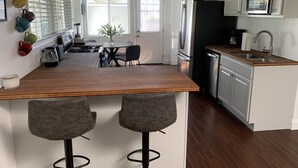 A modern kitchen with a wooden island, two bar stools, a refrigerator, a microwave, and a sink. - Sweet cottage home close to beaches, airport and other attractions (San Diego)
