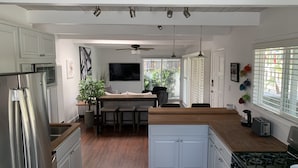 A modern kitchen with white cabinetry, a central island, a stove, and a dining area with a ceiling fan. - Sweet cottage home close to beaches, airport and other attractions (San Diego)