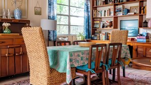 Une pièce chaleureuse avec une table en bois, des chaises, une bibliothèque et une fenêtre avec des rideaux.