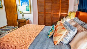 Une chambre à coucher bien rangée, avec un lit, une armoire en bois, une table de chevet avec une lampe et un tableau encadré au mur.