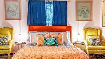 Una cama con cabecera roja, dos sillas amarillas y una manta anaranjada con estampado.