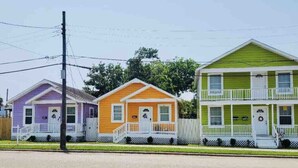 Three colorful houses with front porches, a wooden fence, and a clear sky.