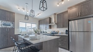 Une cuisine moderne dotée d’un îlot central, d’appareils électroménagers en acier inoxydable et de meubles de rangement en bois.