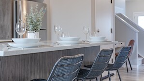Une cuisine moderne avec un îlot central, des meubles de couleur sombre en bois et un escalier en arrière-plan.