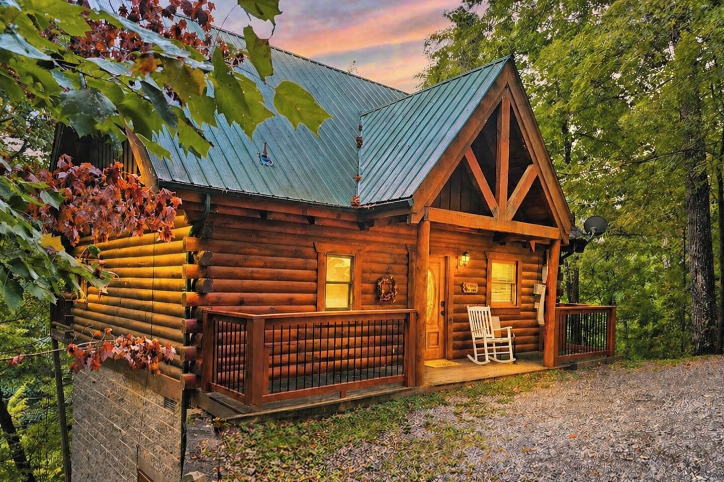 A log cabin with a metal roof, a porch with a chair, and a gravel driveway.