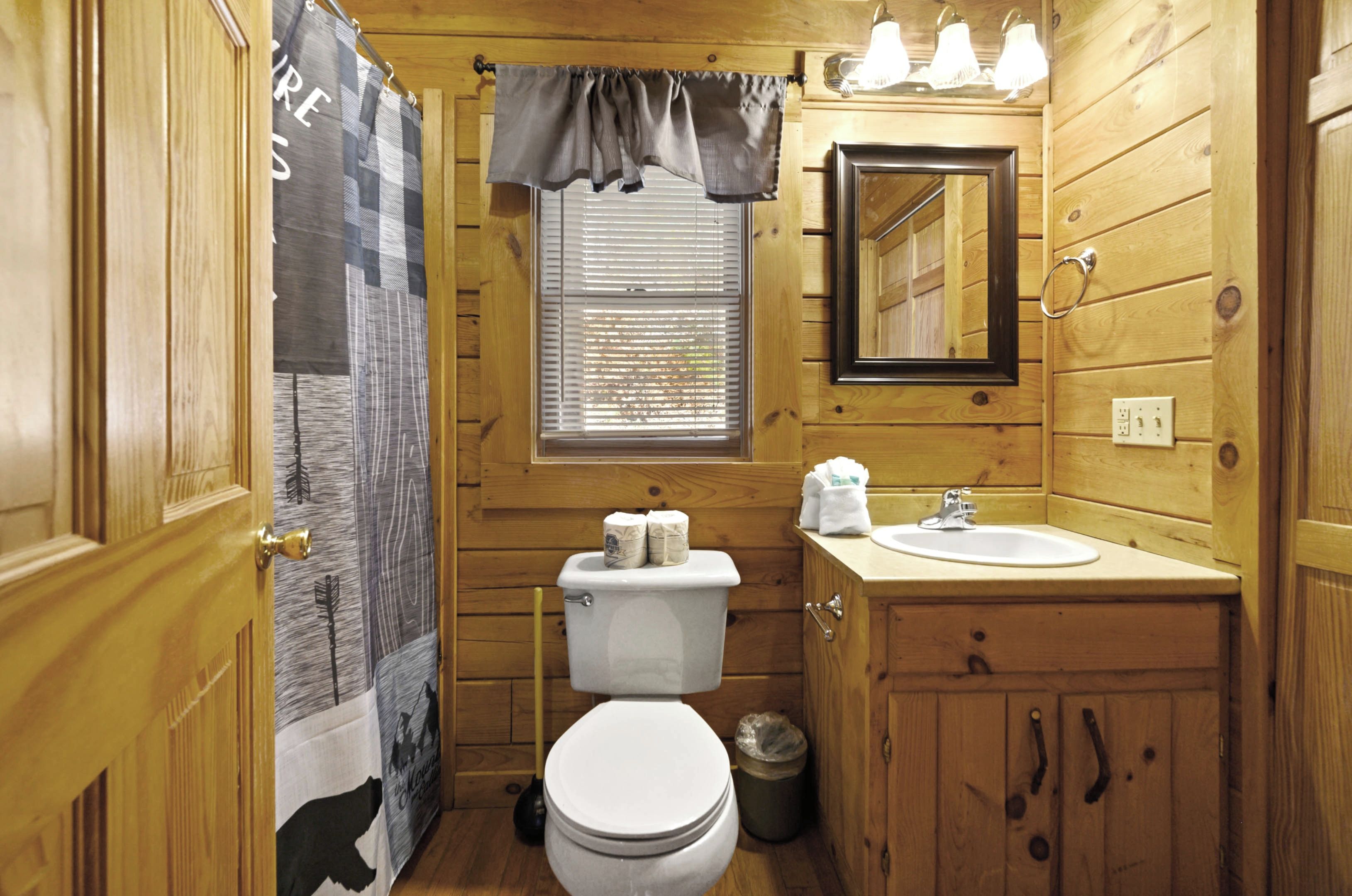 A small, wooden bathroom with a toilet, sink, and mirror.
