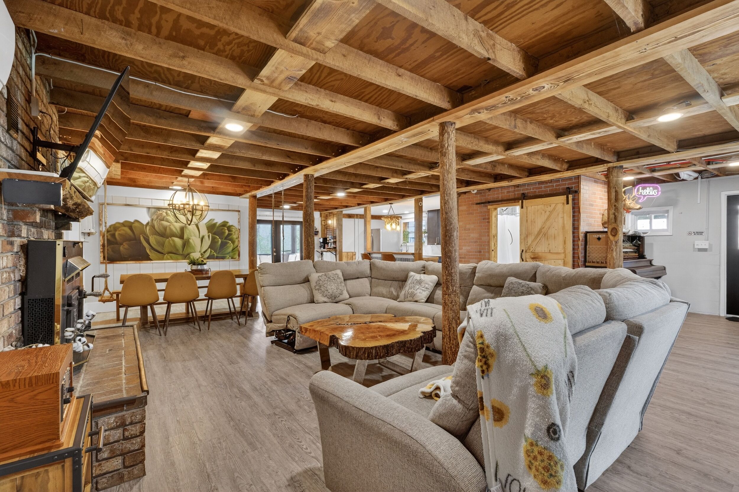 A spacious living area with a high wooden ceiling, a large sectional sofa, a dining table with chairs, and a rustic wooden coffee table.