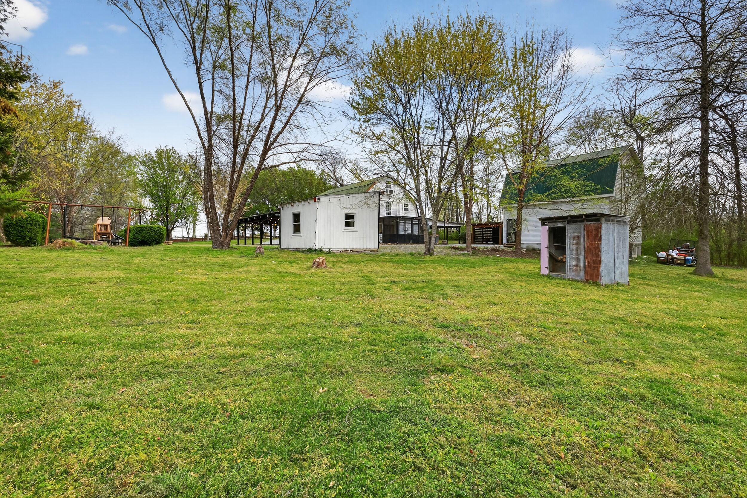 A grassy area with a small white building, a swing set, and trees.