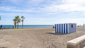 Ein Strand mit einer Holzstege, Palmen und einem kleinen blau-weiß gestreiften Bauwerk.