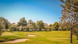 Un campo de golf con búnkeres de arena, cielo despejado y edificios residenciales al fondo.