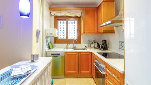 Cocina compacta con armarios de madera, lavavajillas, estufa y una ventana con cortinas decorativas.