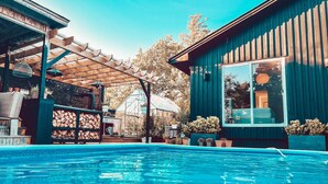 Ein Schwimmbad mit Holzterrasse und einem Gewächshaus im Hintergrund.