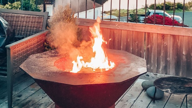 Eine Terrasse mit Feuerstelle, mit Blick auf einen See und bewaldete Hügel.