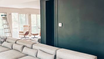 A modern living room with a sectional sofa, a dark accent wall, and a view of the outdoors through large windows.