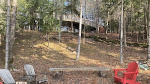 Un área boscosa con una terraza de madera y dos sillas Adirondack rojas.