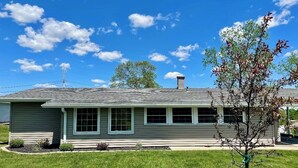 A single-story house with a grey roof and white trim, a chimney, and a small front yard with a tree and shrubs. - Cozy 3 bed, 2 bath home close to historic downtown Hannibal (Hannibal)