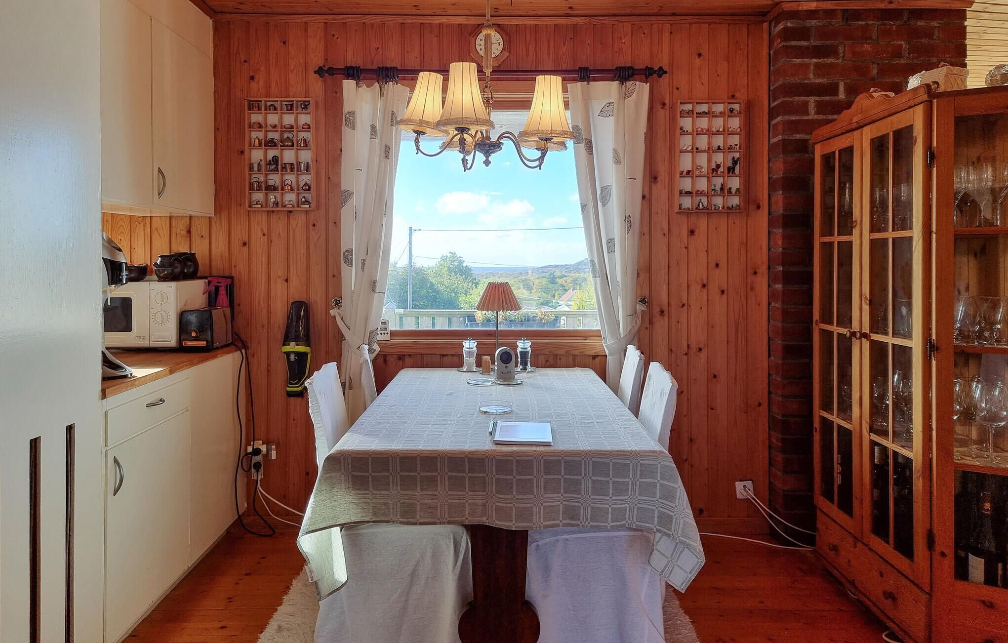 A cozy room with a wooden interior, a dining table with a white tablecloth, a chandelier, and a view of the outdoors.