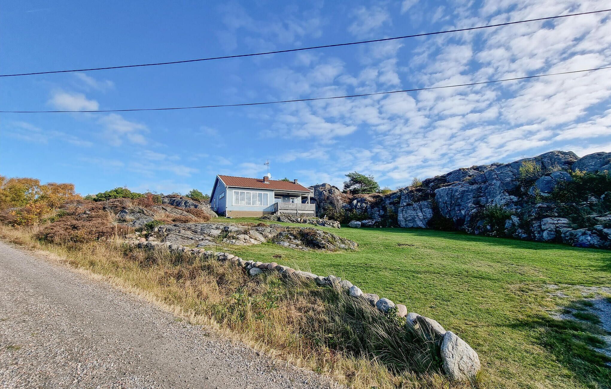 Una casa con tetto rosso, circondata da un prato erboso e un terreno roccioso.