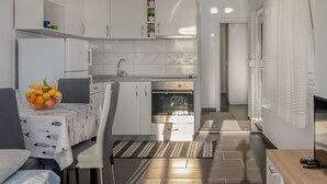 Eine kleine Küche mit weißen Schränken, einem eingebauten Backofen und einem Essbereich mit Tisch und Stühlen.