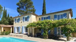 A two-story building with a swimming pool, outdoor seating, and a pergola with vines.