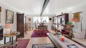 A cozy living room with a wooden dining table, chairs, a bookshelf, a sofa, and a coffee table.
