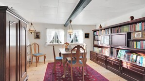 A room with a dining table, chairs, a bookshelf, and a red patterned rug.