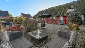 A courtyard with outdoor seating, a thatched-roof building, and a red house with a white door.