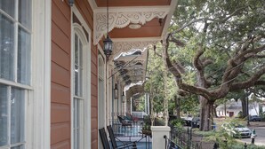 A covered porch with rocking chairs, a railing, and a view of the street and trees.