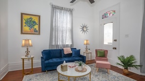 A living room with a blue sofa, a round coffee table, two lamps, a potted plant, and a door with a stained glass window.