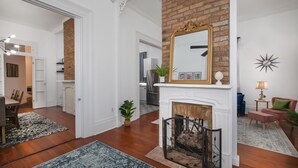A spacious living room with hardwood flooring, a fireplace, a large mirror, and a dining area with a table and chairs.