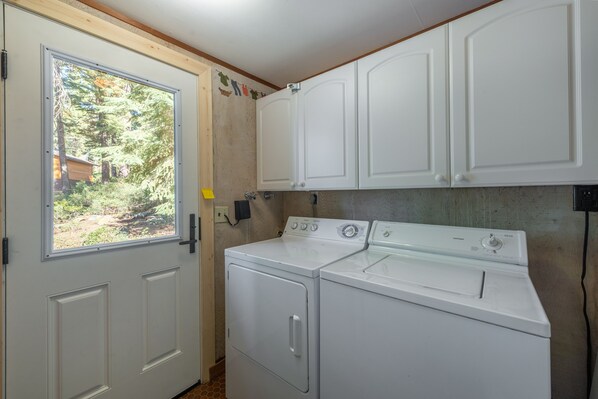 A laundry room with a washer and dryer, wooden cabinets, and a window with a view of trees.