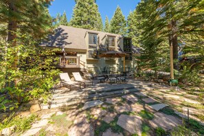 A two-story house with a patio area, surrounded by trees.