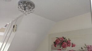 Een plafond met een kroonluchter van kristal, een luchtverwarmingsunit aan de muur en een bloemschilderij.