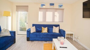 Een woonkamer met een blauwe bank, een witte salontafel en een boekenkast met boeken en een popcornbak.