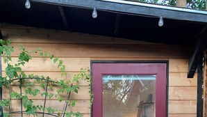 A wooden cabin with a red door, potted plants, and a 'Hello Sunshine' mat. - Family Home Near Bidwell Park (Chico)