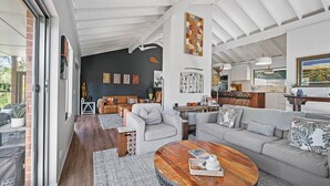 Ein modernes Wohnzimmer mit einer großen Couch, einem Couchtisch und einem Essbereich, wobei im Hintergrund eine Küche zu sehen ist.
