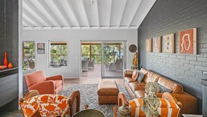 Ein geräumiges Wohnzimmer mit modernem Design, ausgestattet mit einer großen Couch, einem Couchtisch und einem Kamin. Große Fenster sorgen für natürliches Licht und bieten einen Blick ins Freie.
