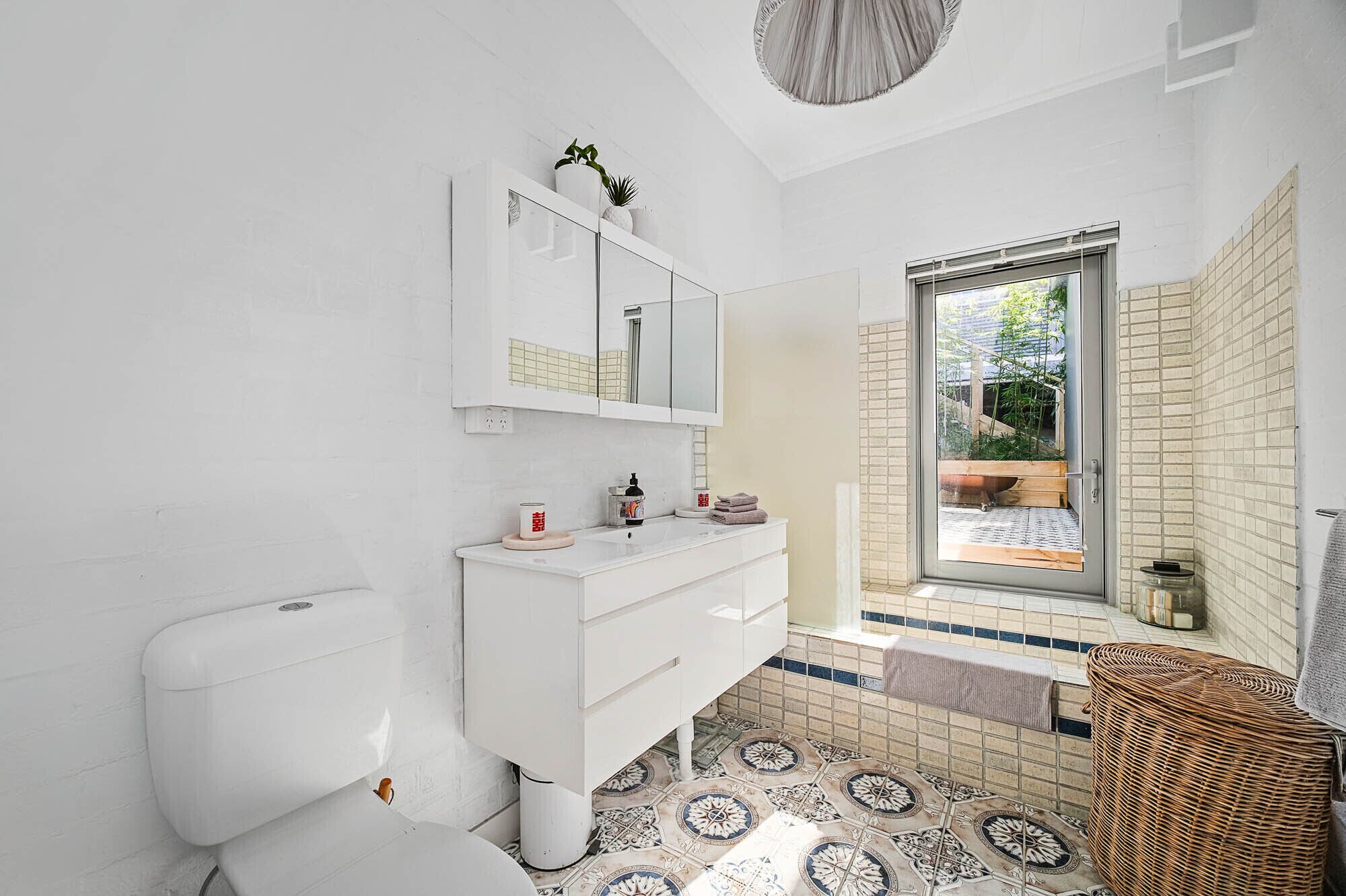 A modern bathroom with a white vanity, a large mirror, and a view of an outdoor garden through a glass door.